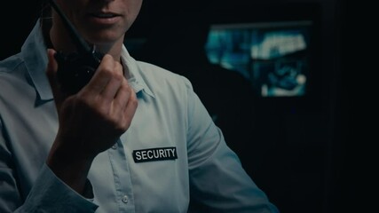 Medium midsection shot of anonymous female security guard in uniform shirt, with badge answering call on portable radio while watching CCTV surveillance screens in control room