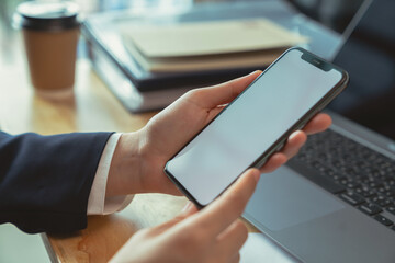 Businessman hand holding black smartphone with blank screen on desk in the office.