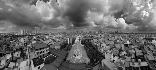Obraz premium French Colonial Church and Ho Chi Minh City Skyline View in black and white. Church in high density urban area aerial rooftop view with city skyline and dramatic sky.