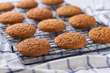 Freshly baked oatmeal cookies cooling on a black wire rack, with in a light kitchen table, selective focus.