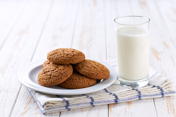 Tasty oatmeal cookies and glass milk on a light kitchen table, selective focus.