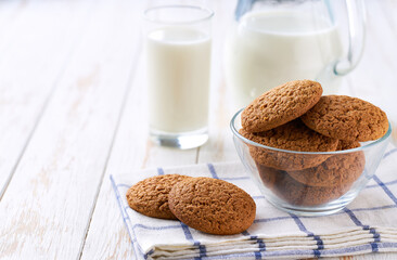 Glass and a jug of fresh milk with oatmeal cookies on a on a white table,selective focus.