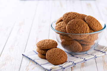 Tasty oatmeal cookies round shape in a clear glass bowl  with on a light kitchen table, selective focus.