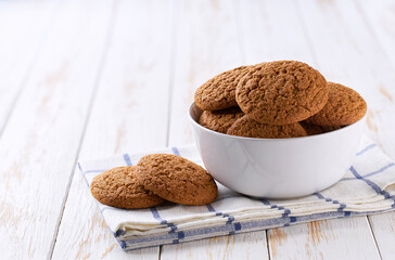 Round oatmeal cookies in a ceramic bowl on a white table, selective focus.