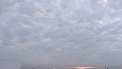 Fototapeta na wymiar The sky was cloudy with a blue, gray, and pink shades. The clouds expand and cover most of the sky. The sunrise is rising in the distance, throwing warm light in the clouds.