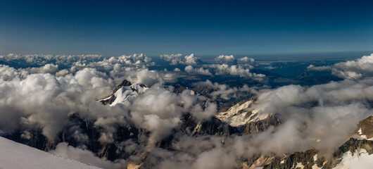Panorama view Alpine tops from Mont Blanc glacier at morning, low clouds and clear blue sky