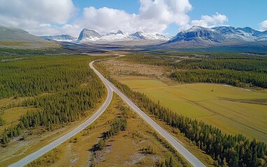 Aerial view of a winding road through a valley with snow-capped mountains in the distance.