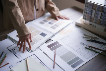 Female architect choosing color swatch sample to design interior of building project on blueprint