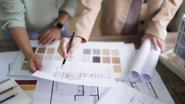 Two female architects discuss and brainstorm about interior designing building project on blueprint