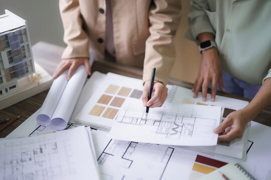 Two female architects discuss and brainstorm about interior designing building project on blueprint