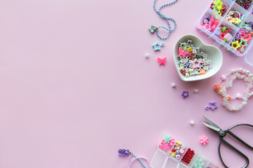 Crafting colorful beaded jewelry with charms and scissors on a pink surface in a creative workspace