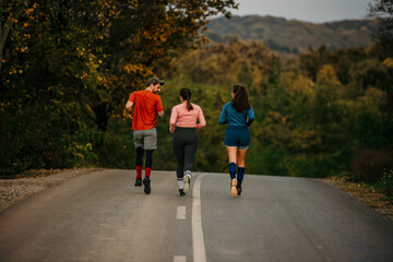 Rear view of a group of athletic young adults are running across the country road