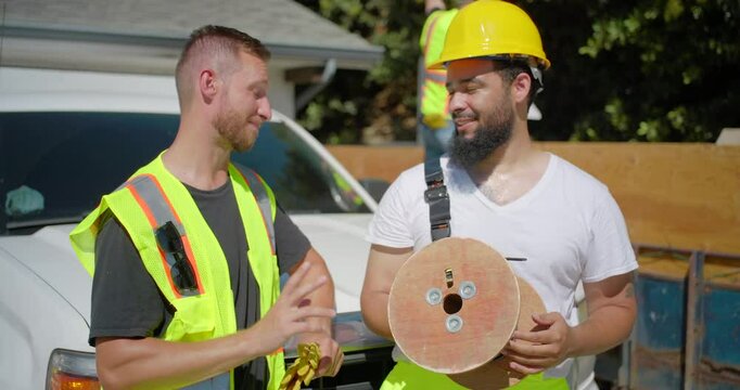 In a vibrant construction site during a house remodeling project, two cheerful construction workers, one adorned in a bright safety vest and helmet, are engaged in a lively conversation