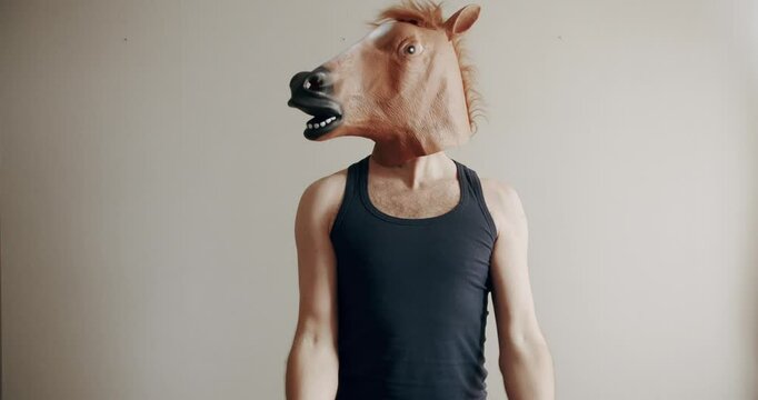 Funny man with horse mask doing exercise with weights for hand training on the white background at home. Comical fitness at home. Humorous stretches. Funny home workout.