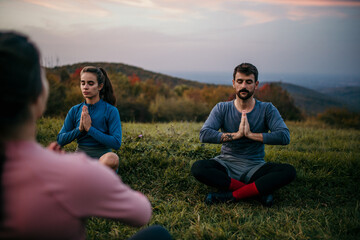 Fit sporty people practicing yoga and meditating during a late sunset period of a day outdoors