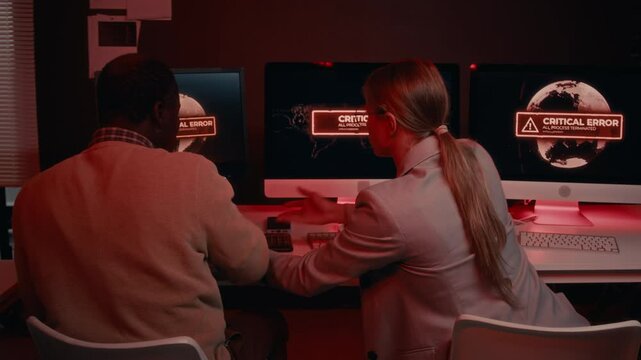 Medium rear shot of multiethnic male and female IT security specialists arguing and frantically typing commands on keyboards while trying to defend breached corporate system from hacking attack