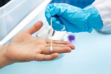 Scientist's hand holding a cotton swab and wiping dipped in diluted rubbing alcohol to hands and fingers. Cleaning dirty fingers to test for disease for food safety is a process of measuring in lab.