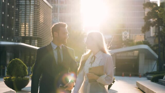 Smiling businessman and business woman talking on the go in setting sun sunlight, slow motion