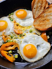 Fried eggs with tomatoes on a cast iron frying pan on a wooden background