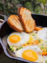 Fried eggs with tomatoes on a cast iron frying pan on a wooden background