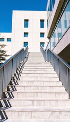 Modern concrete stairs with stainless steel railings leading up to a building with a blue sky.
