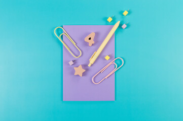 Top view of purple notebook on blue background. Paperclips, pen, number, shape and pins. School, office wallpaper. Flat lay, copy space.