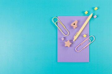 Top view of purple notebook on blue background. Paperclips, pen, number, shape and pins. School, office wallpaper. Flat lay, copy space.