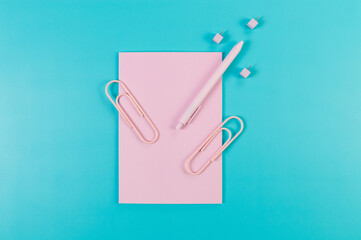 Top view of pink notebook on blue background. Paperclips, pen and pins. School, office wallpaper. Flat lay, copy space.