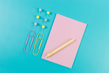 Top view of pink notebook on blue background. Paperclips, pen and pins. School, office wallpaper. Flat lay, copy space.