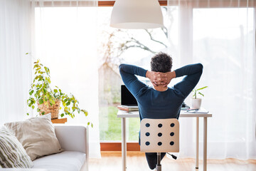 Homeoffice for handsome man. Rear view of man sitting on office chair with hands behind head,...