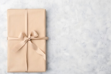 Elegant gift box wrapped in brown paper with beige ribbon on marble background