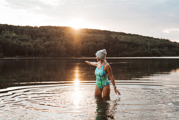 Cold water swimming for elderly women. Senior sporty women standing in lake during cold morning, looking at sunrise.