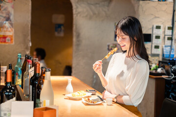 一人でカウンター席に座って焼き鳥を食べる女性
