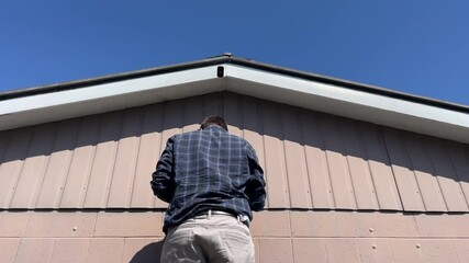 Middle aged caucasian man adjusting a home security camera mounted just below the roof of an old 1970's house in New Zealand