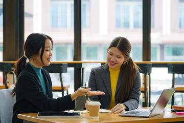 Two young Asian businesswomen discussed investment project work and planning strategy. Business people talk together on laptop computers at the office.