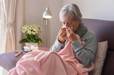 Senior caucasian woman blowing nose with severe cold and fever symptoms like seasonal flu, covid or...