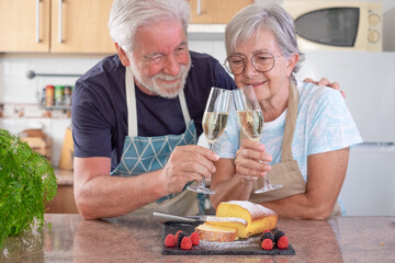 Defocused senior couple in the home kitchen toasting with white wine ready to eat the homemade plumcake.. Cooking at home for family concept