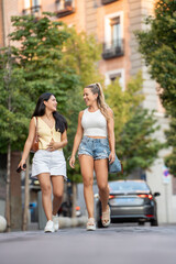 Two young women are enjoying a summer day walking down a city street and talking