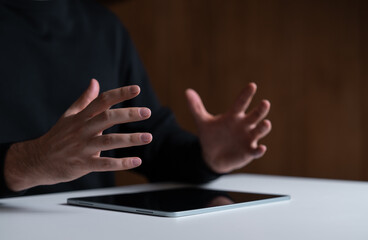 Hands gesturing above a tablet on a white table with a dark background.