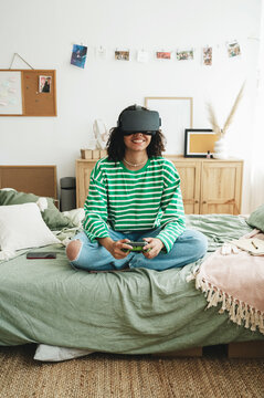 Smiling teenage girl wearing virtual reality simulators playing video game at home