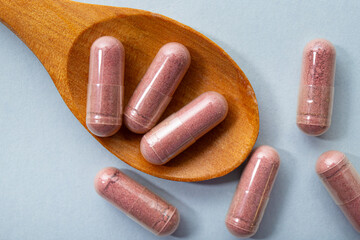 Cranberry or Vaccinium subg. Oxycoccus powder supplement capsules on wood spoon, studio shot...