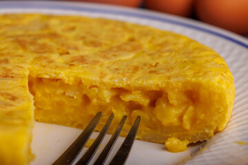 Close-up of a sliced Spanish omelette with bread, eggs, and a red checkered napkin on a textured blue concrete surface