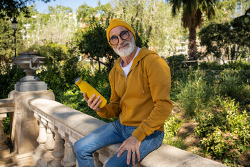 Smiling senior man wearing knit hat sitting with water bottle on wall