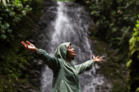 Woman with arms outstretched standing in front of waterfall
