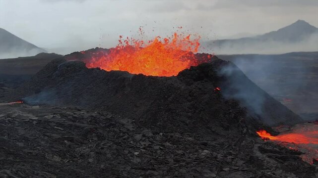 Super slow-motion aerial footage capturing an active volcanic eruption with lava violently exploding from the crater and flowing down the rugged terrain in Iceland near Reykjavik.