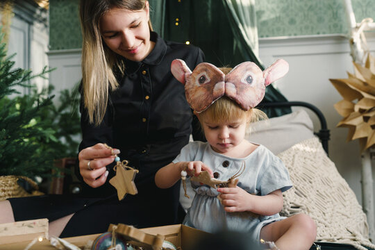 Smiling mother and daughter sitting with Christmas ornaments in box on bed at home