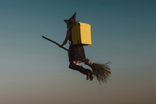 Woman wearing witch costume with yellow delivery backpack and flying in sky