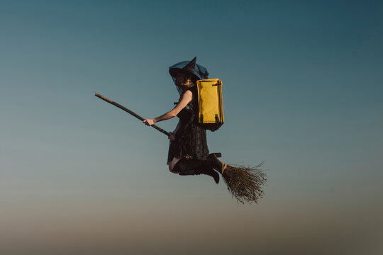 Woman wearing witch costume with delivery backpack and flying in sky
