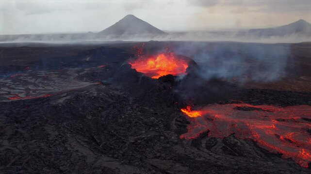Aerial shot of an active volcanic eruption in Iceland, showcasing glowing lava streams flowing from the crater and thick smoke rising into the sky.