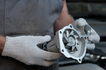 Replacement of the water pump in the car engine. An auto mechanic holds a new water pump, monitors...